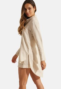 Beige linnen shirt met een kraag, lange mouwen en een gebogen zoom. Beschikt over zijsplitten en een relaxte pasvorm.