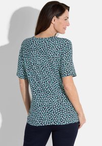 Haut à motif floral avec des manches courtes, présentant un fond noir et de petites fleurs turquoise. Tissu doux et léger.