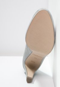 Chaussure à talon haut en daim gris clair avec un bout pointu, texture lisse et semelle en caoutchouc dotée de rainures horizontales pour une bonne adhérence.