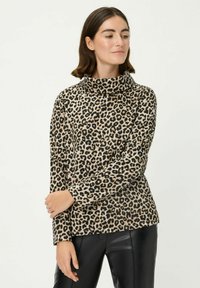 Leoprint Rollkragenpullover in Beige und Schwarz, aus weichem Stoff, lockere Passform, lange Ärmel. Kombiniert mit schwarzen Lederhosen.