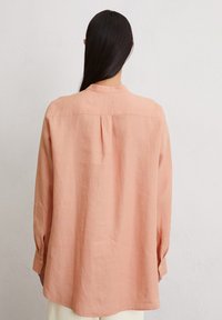 Lichtroze linnen shirt met een rugplooitje, knoopmanchetten en een relaxte pasvorm; heeft een minimalistisch ontwerp en een gestructureerde stof.