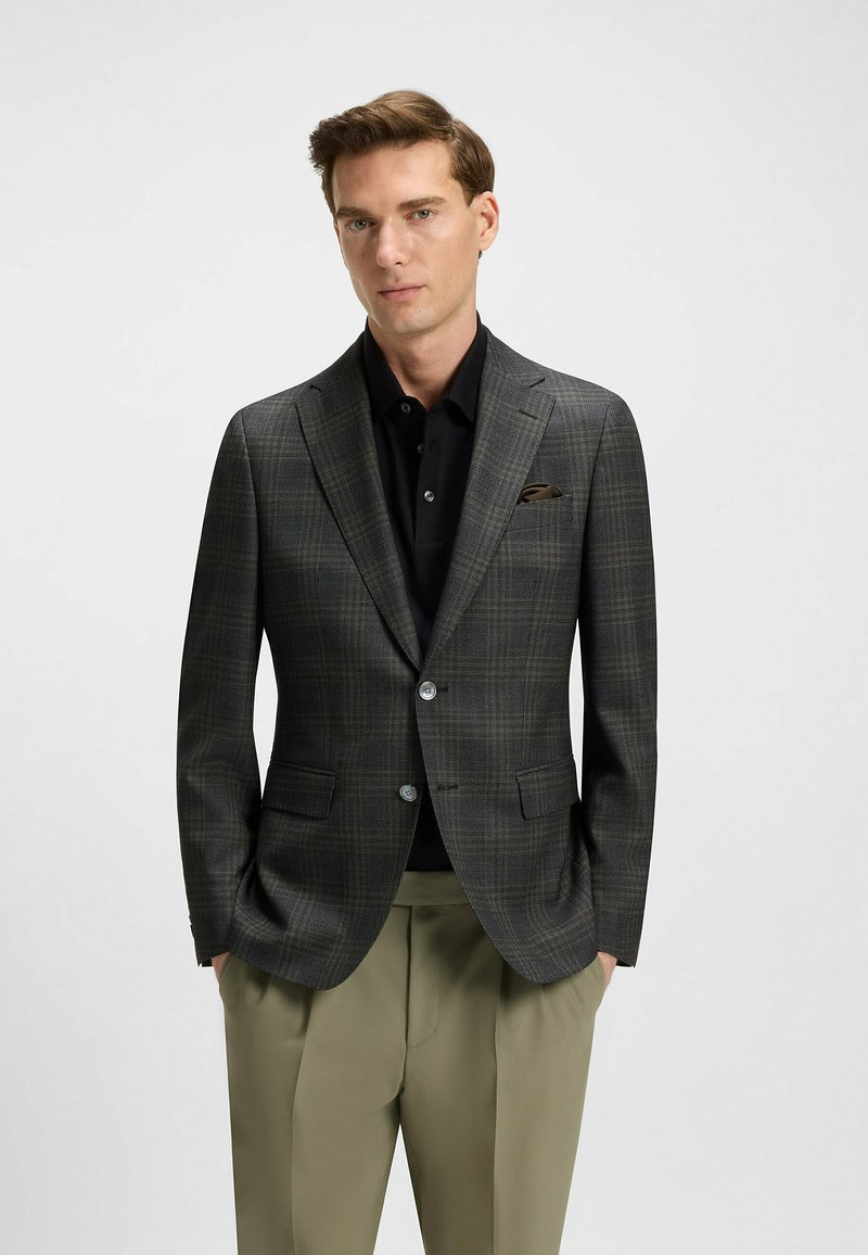 Czarny żakiet w kratę w odcieniach szarości i brązu, z dwoma guzikami, klapami w szpic i dwiema kieszeniami z przodu. Nosi się go na czarnej koszuli.