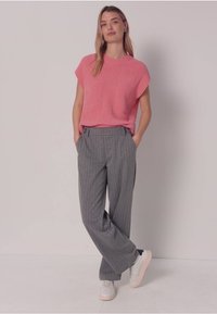 Růžový pletený top s krátkými rukávy a šedé široké kalhoty s proužky, doplněné světlými teniskami; model stojí s rukama v kapsách.