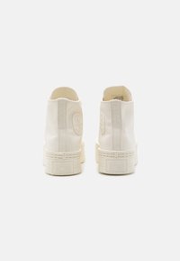 Vysoké plátěné tenisky v off-white barvě s texturovaným povrchem, gumovými podrážkami a raženým logem All Star na zadní straně, který zahrnuje detaily šití.