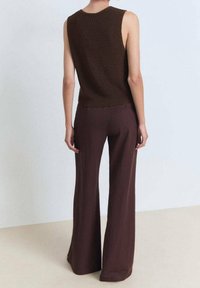 Brązowy bezrękawnik dzianinowy w połączeniu z brązowymi spodniami o szerokich nogawkach, charakteryzującymi się luźnym krojem i gładką fakturą. Prosty design, bez widocznych wzorów.