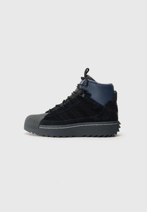 Czarno-granatowy, wysokostający sneaker z grubą, żłobioną podeszwą, sznurowanym fasonem i teksturowanym czubkiem na neutralnym tle.