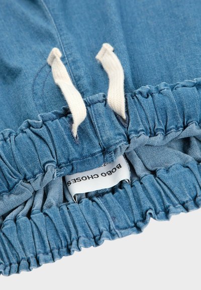 Pantalones cortos de mezclilla azul con una cintura fruncida, que cuentan con cuerdas de ajuste color crema y una etiqueta visible que dice "Bobo Choses". Textura suave.