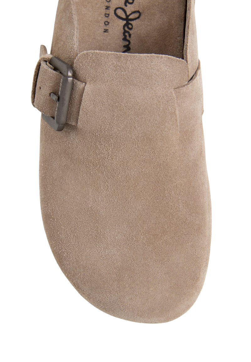 Sabot en daim beige avec une large sangle et une boucle en métal sur le côté, présentant un bout arrondi et une semelle intérieure rembourrée.