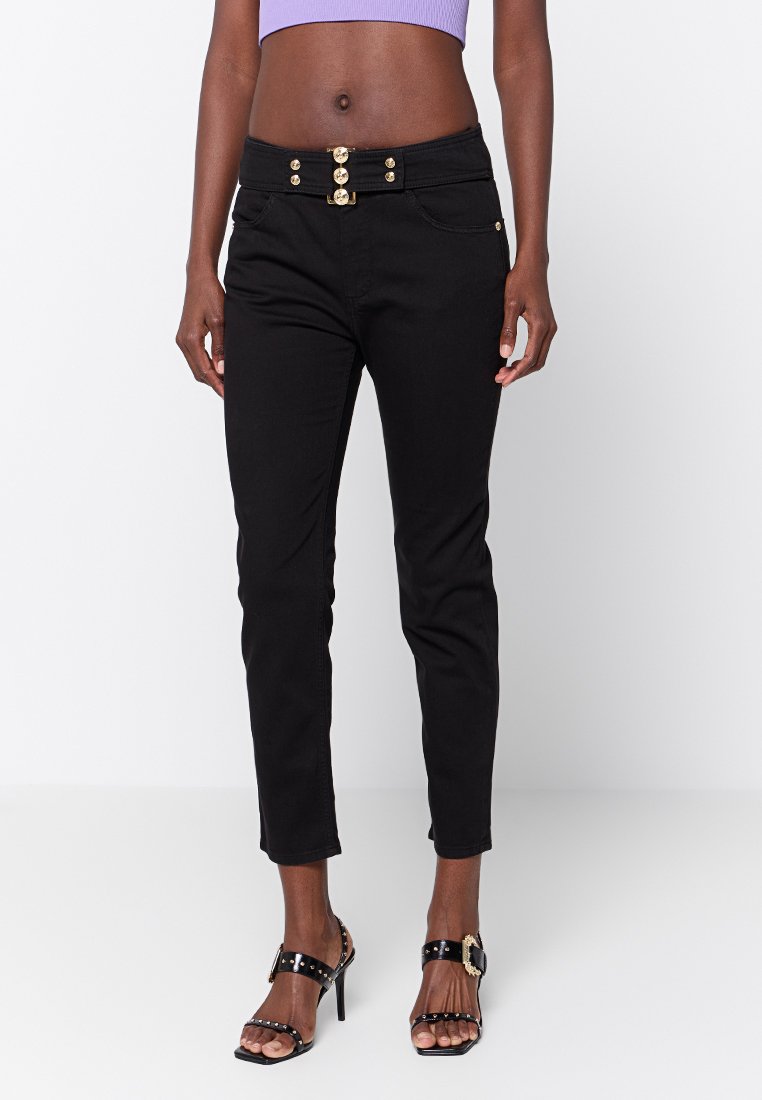 Czarne, krótkie dżinsy z guzikiem i złotymi elementami, oraz dwiema przednimi kieszeniami, zestawione z czarnymi sandałami na obcasie.