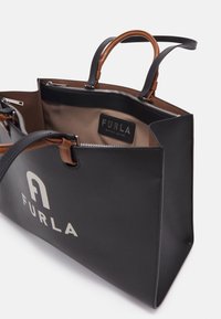 Czarna skórzana torba tote Furla z brązowymi uchwytami, otwartym zamkiem błyskawicznym, beżowym wnętrzem oraz białym logo Furla z przodu.