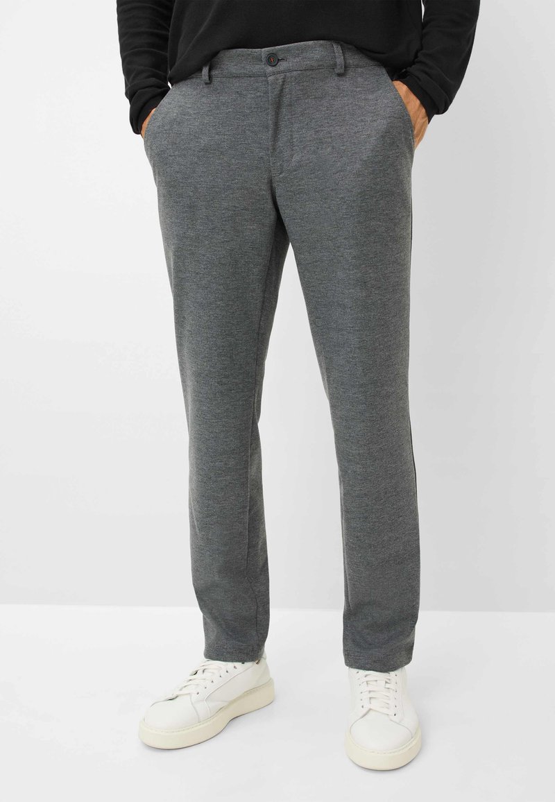 Pantalon gris ajusté en tissu texturé avec une taille boutonnée, des poches latérales et une coupe slim, associé à des baskets blanches.