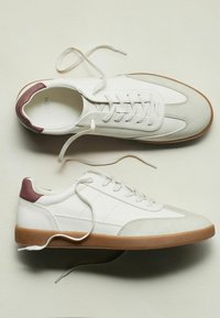 Hvide sneakers med en glat læderoverdel, grå ruskindsdetaljer og brun gummisål. Har snørebåndsdesign og diskrete perforeringer.