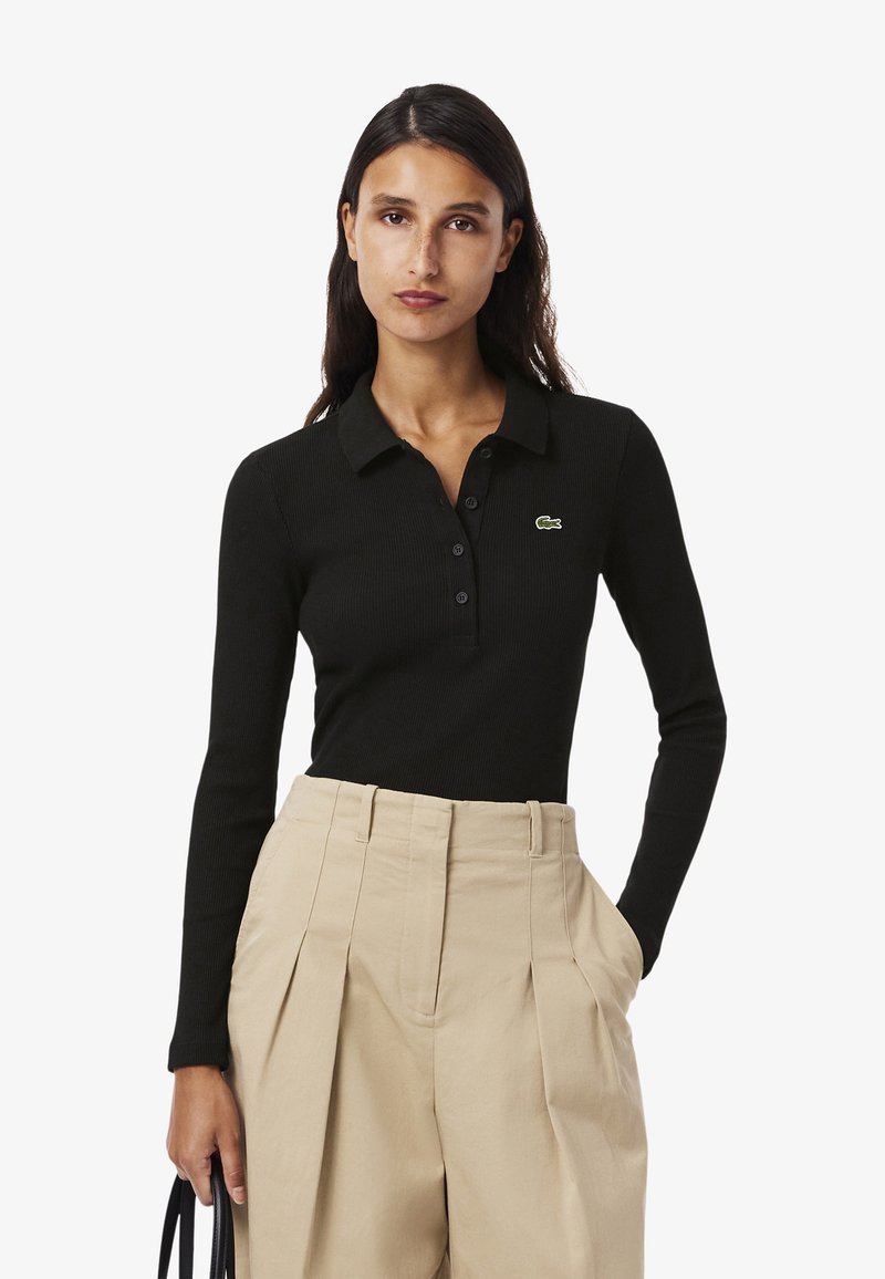 Svart långärmad polo med ribbad textur, med en placket med tre knappar och en grön broderad krokodil-logotyp.