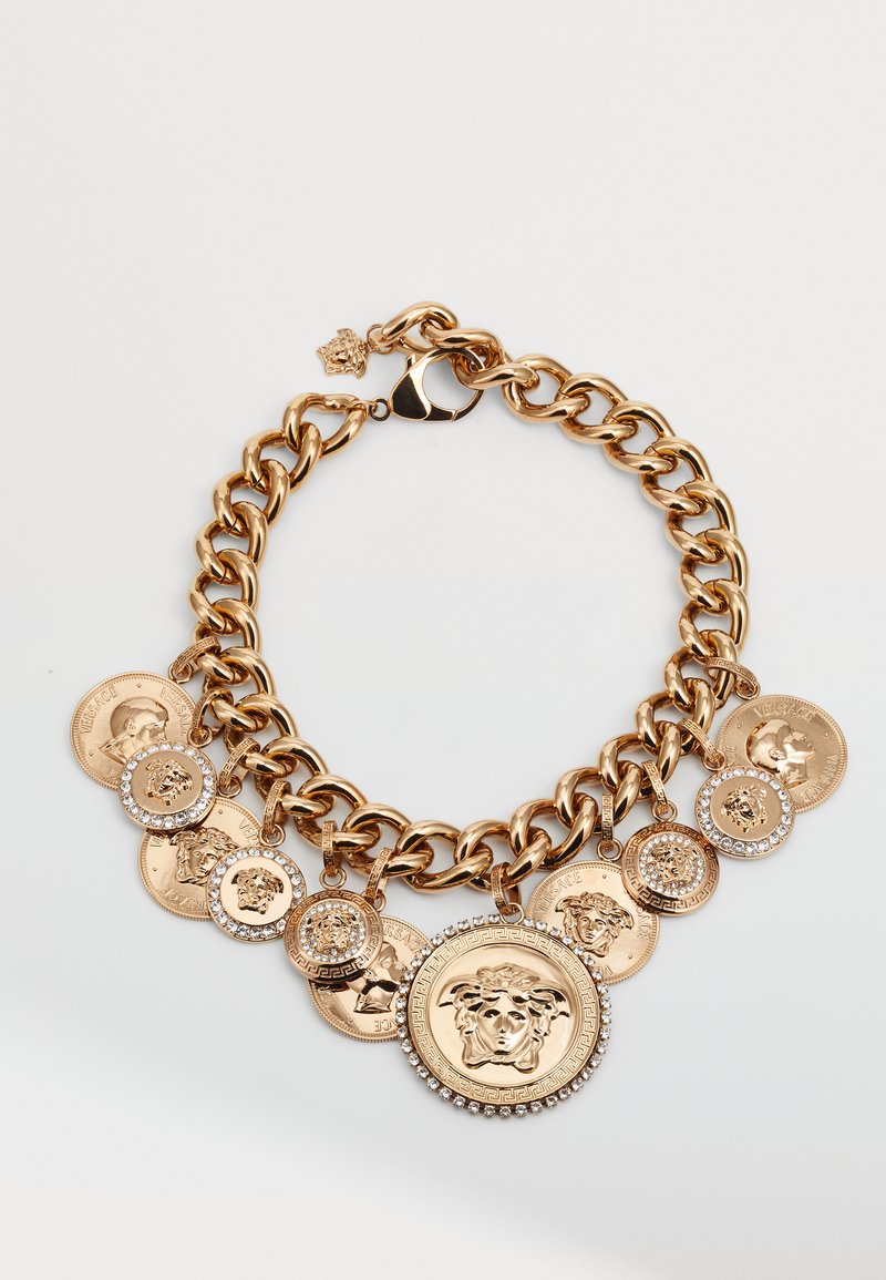 Zlato-tonirana debela verižica z zbirko dekorativnih kovancev in velikim osrednjim medaljonom s kamni v svetlobi.