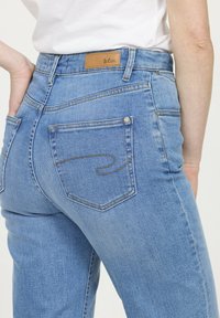 Jean en denim bleu clair à taille haute, avec une étiquette en cuir marron et des coutures décoratives sur les poches arrière.