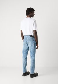 Jeans de color azul claro con un corte relajado, que presentan un diseño de cinco bolsillos y un acento en la cinturilla negra, combinados con una camiseta blanca y zapatos negros.