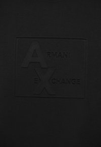 T-shirt nera con logo in rilievo che presenta la scritta "ARMANI EXCHANGE" e le lettere "A" e "X" in un design rettangolare.