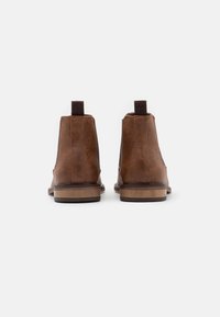 Bottes cheville en cuir marron avec une texture lisse, des panneaux latéraux élastiques et une languette de tirage. Talon légèrement surélevé et semelle en caoutchouc contrastante.