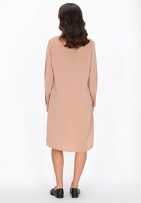 Langärmliges, einfarbiges Blush-Kleid aus weichem Stoff, mit lockerer Passform und Knopfakzenten an den Bündchen. Tragen mit schwarzen, flachen Schuhen.