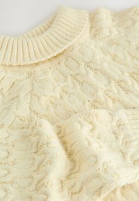 Creme farvet kabelstrikket sweater med et tekstureret design og ribbet krave. Stoffet ser blødt og varmt ud, med synlige detaljer i hele. 