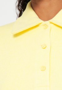 Polo amarelo canelado com gola clássica e cinco botões combinando, com textura suave.
