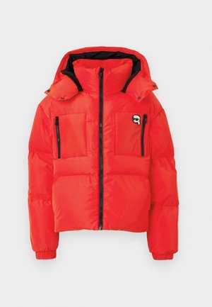 Rote Pufferjacke mit Kapuze, ausgestattet mit einem hohen Kragen, schwarzen Reißverschlüssen und zwei Brusttaschen vorne. Hergestellt aus einem glänzenden, gesteppten Material.