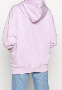 Felpa rosa chiaro con una vestibilità comoda, dotata di cappuccio con coulisse e polsini a costine. Indossata con jeans in denim blu chiaro.