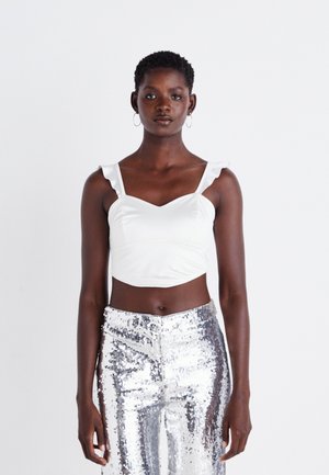 Top bianco corto con spalline a balze, abbinato a pantaloni in paillettes argentate lucide. Tessuto morbido con design aderente e scollatura a V.