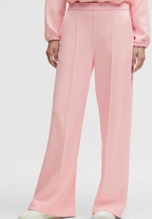 Persona che indossa pantaloni rosa a vita alta e gamba larga con cuciture frontali e una maglia rosa a maniche lunghe abbinata, completati da scarpe bianche.