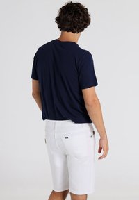 Camiseta de algodón azul marino combinada con pantalones cortos de mezclilla blanca. Los pantalones cortos presentan un parche con el logo y un diseño clásico de cinco bolsillos.