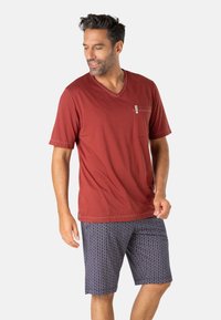 T-shirt rouge à col en V associé à un short bleu marine à motifs. Le t-shirt présente une poche sur le côté gauche de la poitrine et des manches courtes, avec une texture décontractée et douce.