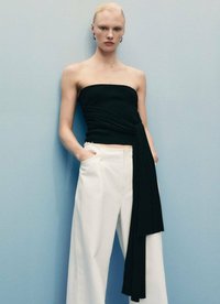 Top nero senza spalline con dettaglio attorcigliato, abbinato a pantaloni bianchi a gamba larga. Texture morbide e linee pulite creano un look moderno.