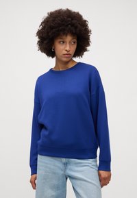 Felpa blu realizzata in tessuto morbido con una vestibilità comoda, scollo rotondo e maniche lunghe. Abbinata a jeans azzurri.