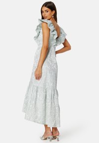 Mentolově zelené šaty z texturované látky s volánovými ramínky a vrstveným lemem, doplněné o stříbrné podpatky.