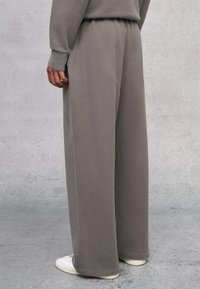Grau weite Hosen aus weichem Material mit elastischem Bund. Sie haben eine glatte Textur und seitliche Taschen, kombiniert mit weißen Sneakers.