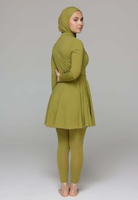 Olijfgroen, aansluitend jurkje met lange mouwen, gecombineerd met bijpassende leggings. Zachte textuur, rok tot op de knie en een bijpassende hoofddoek.