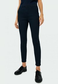 Marinblå, texturerade byxor med en åtsittande design, midjahöjd och fickor, ihop med svarta snörskor.