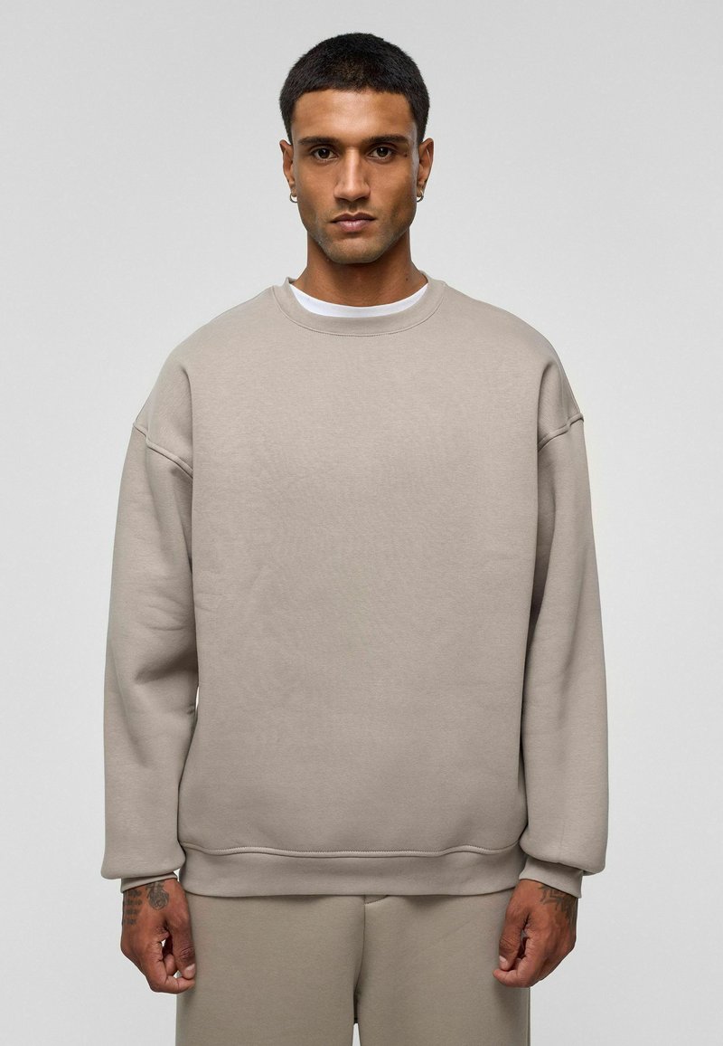 Beige sweatshirt met een ronde hals, verlaagde schouders en geribbelde boorden. Gemaakt van zachte stof, met een eenvoudig, minimalistisch ontwerp.