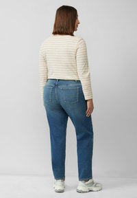 Licht gestreepte blouse met lange mouwen, gecombineerd met middelwassing jeans met rechte pijpen. De outfit wordt compleet gemaakt met witte sportschoenen.