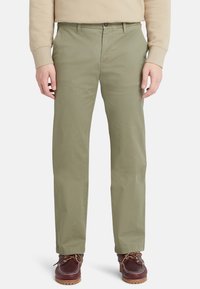 Chinos de algodón verde oliva claro con ajuste recto, que cuentan con cierre de botón, bolsillos laterales y se combinan con zapatos marrones de cordones.