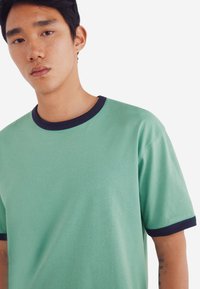 Mintgrøn T-shirt med en marineblå ribbet krave og ærmekanter. Fremstillet af blødt stof, har den en afslappet pasform og en glat overflade.