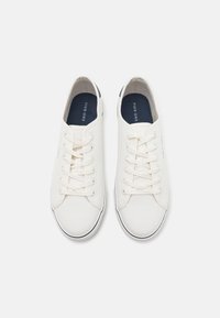 Zapatillas de lona en color blanco roto con punta redonda, que cuentan con cordones blancos, forro interior azul marino y borde de suela de goma negra.