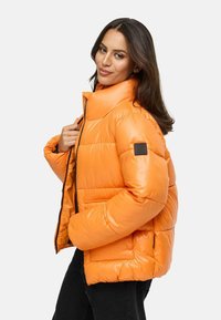 Gevoerde winterjas in fel oranje, met een hoge kraag, ritsluiting, zijzakken en zwart logo-opdruk op de linkerarm.