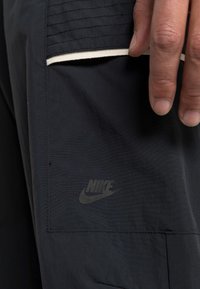Svarta Nike träningsshorts med en synlig ficka och en diskret logotyp. Tyget är slätt med en lätt lyster och ett texturerat midjeband.