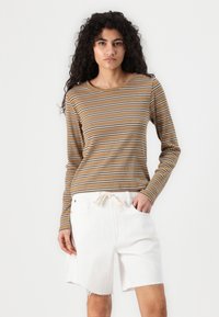 Langermet stripet topp i brunt, kremfarge og mørkebrun, med rund hals og ribbet tekstur, paired med hvite denimshorts.