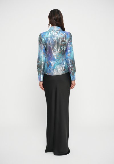 Saia longa preta com uma silhueta ajustada, combinada com uma blusa colorida, estampada e brilhante, apresentando padrões em espirais nas cores azul e prata.