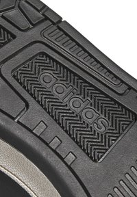 La semelle de la chaussure Adidas est en caoutchouc noir avec une texture antidérapante, un logo en relief et un motif de semelle en zigzag pour une meilleure traction.
