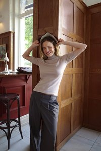 Top de tubo beige claro, de media manga, combinado con pantalones de pierna ancha en gris oscuro. Entorno interior con paneles de madera y un bar.