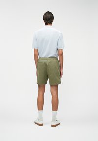 Polo shirt léger bleu à manches courtes, short vert avec taille élastique, deux poches arrière et baskets blanches sur un fond neutre.