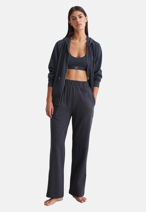 Donkergrijze sportoutfit met een ritsjack, een aansluitende sportbeha en losse broek met een elastische tailleband. Minimale branding zichtbaar.